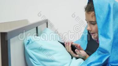 十几岁的女孩在毯子下玩智能手机。 睡前小女孩躺在床上上网