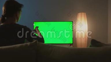 女人坐在沙发上，用绿色屏幕看电视，用遥控器<strong>切换</strong>频道。彩色键
