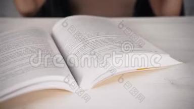 女孩坐在一张白色的桌子上，戴着眼镜看着一<strong>本书</strong>，日记。 视力不好。