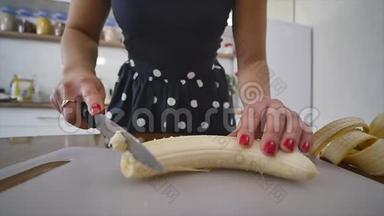 女人在家庭厨房的木制厨房板上切香蕉。 在家做饭。 厨房里的家庭气氛