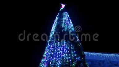 在大雪纷飞的冬夜，大圣诞树上装饰着发光的花环。 相机飞来飞去