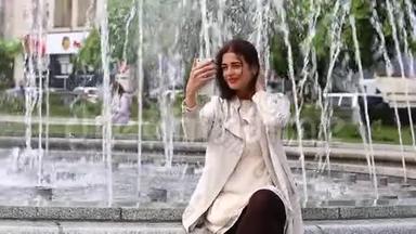 女孩用智能手机笑的肖像。 在喷泉背景上带着手机的漂亮年轻女人。 很幸福的女人