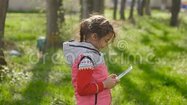 春天，在森林里绿草如茵的背景下，在网游中玩平板电脑的少女