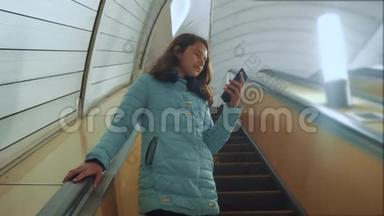 少女生活方式地下地铁乘坐自动扶梯，手持智能手机。 小女孩，黑发女儿
