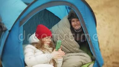 河岸上的旅游帐篷。 两个女孩坐在帐篷附近吃喝看着河。