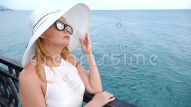一位身穿白色宽边帽子和<strong>太阳镜</strong>的优雅<strong>女士</strong>欣赏海景。 4k，慢镜头