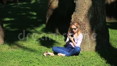 英俊的女人坐在棕榈树下，用智能手机上网