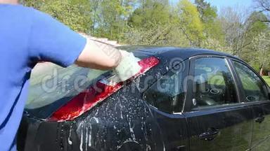 男人用泡沫和海绵清洗黑色最爱的汽车