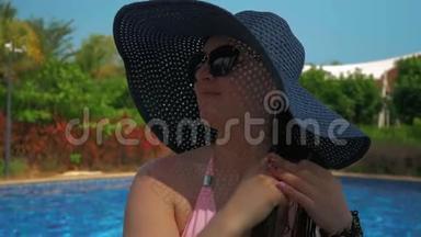 游泳池边戴蓝帽子的漂亮女孩。 夏日的阳光。 慢动作