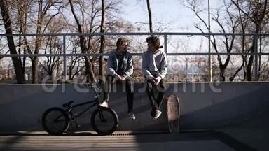 两个朋友的前视图滑板运动员和bmx骑手一<strong>起坐</strong>在城市滑板公园的高栏杆上