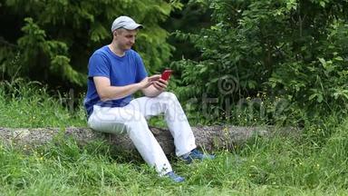 一个戴着红色智能手机的人坐在森林里的一棵倒下的树上