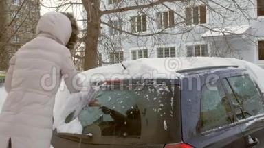 女青年在暴风雪后用刮泥机清洗汽车