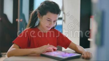 小女孩在玩数字平板电脑。 小女孩坐在桌子旁，在网游社交媒体上玩数字平板电脑