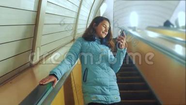 少女生活方式在地下地铁乘坐自动扶梯，手持智能手机。 小女孩，黑发女儿