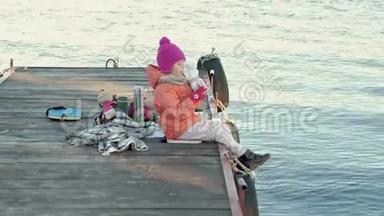 小女孩，穿着暖和的衣服，坐在河岸上，坐在河<strong>港</strong>上，喝热<strong>茶</strong>，野餐