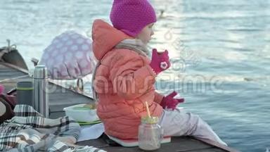 小女孩，穿着暖和的衣服，坐在河岸上，坐在河<strong>港</strong>上，喝热<strong>茶</strong>，野餐