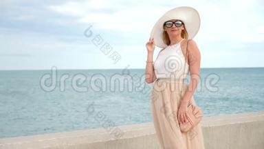 一位身穿白色宽边帽子和太阳镜的优雅女士欣赏海景。 4k，慢镜头
