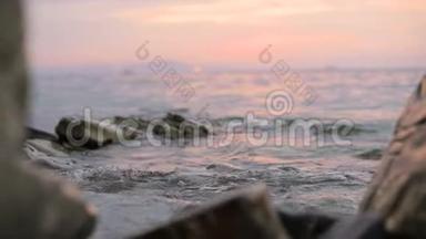 特写慢动作低角度小海浪在岩石海滩上翻滚.. 海边。 傍晚在卵石岩石海滩上日落