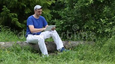 一个带着平板电脑的人坐在森林里一棵倒下的树上