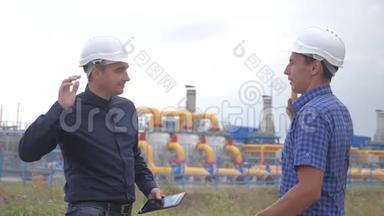 团队合作。 工业煤气生产站的概念。 慢动作视频。 两名戴头盔的工程师在煤气上握手