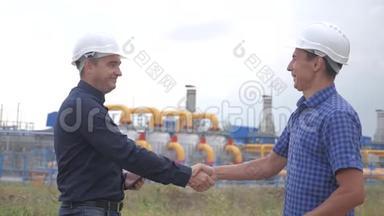 团队合作。 工业煤气生产站的概念。 慢动作视频。 两名戴头盔的工程师在煤气上握手
