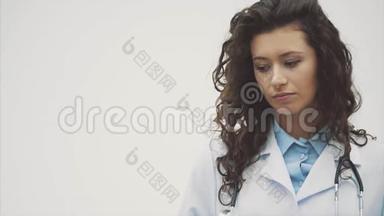 幸福的年轻微笑女孩医生的肖像。 穿着白色长袍。 <strong>双手交叉</strong>站在灰色的