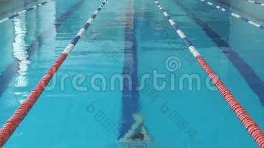 泳镜和泳帽的年轻女子在蓝水室内泳池泳蝶泳