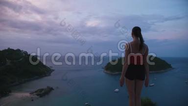 女人在高处练习瑜伽健身运动，日出时可以看到令人惊叹的岛屿景观
