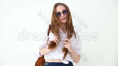 现代青年的时尚。 穿着牛仔裤、白衬衫、带皮背包和眼镜的时髦女孩在白色墙上摆姿势
