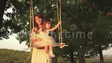 <strong>妈妈</strong>在阳光下摇着女儿在树下摇摆。 特写镜头。 孩子又笑又高兴。 <strong>妈妈</strong>和<strong>宝宝</strong>骑在绳子上