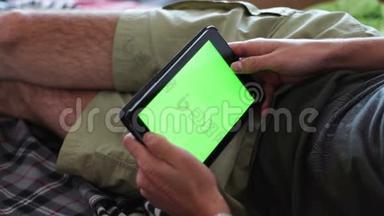 男人躺在家里的沙发上，看着有绿色屏幕的平板电脑