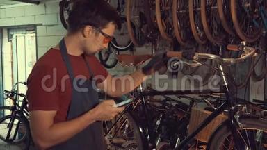 主题小企业自行车修复.. 年轻的白种人黑发男子，戴着安全护目镜，手套，使用移动电话