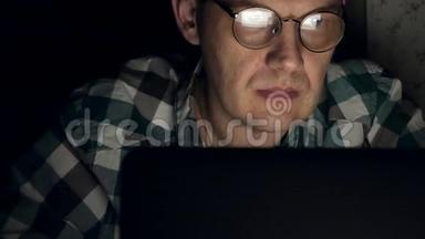 戴眼镜的人工作到深夜。他看起来很担心，他在面前的电脑屏幕上看到一个特写镜头