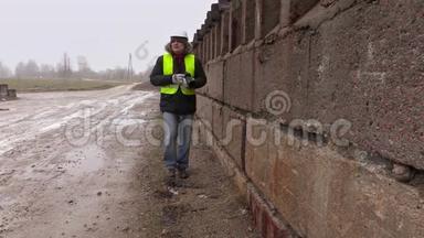 施工工程师在专业摄影摄像上拍照，并在混凝土墙附近行走