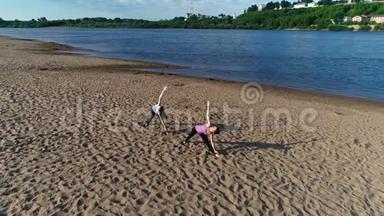 两个女人在城市河边的沙滩上做瑜伽。 日出时美丽的城市景色。