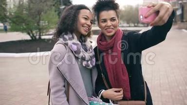两个可爱的非裔美国女人带着购物袋和微笑自拍。 朋友们在参观商场销售后玩得很开心。