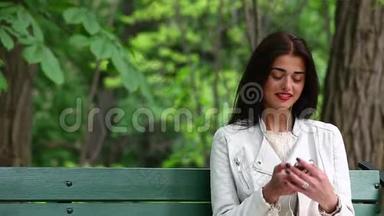 一位女士在公园里听着一部带耳机的智能手机里的音乐，一位美丽的女士用带耳机的智能手机听音乐