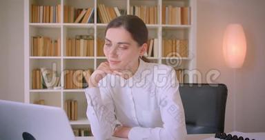 一位年轻迷人的高加索女商人在<strong>办公室里</strong>用笔记本电脑拍摄的特写肖像，<strong>办公室里</strong>放着书架