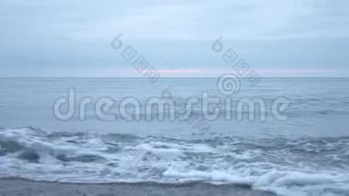 日落时的卵石海滩。 波浪飞溅，碎成飞沫.. 4k，慢动作