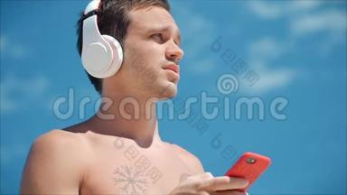 英俊的年轻人用无线耳机听他的智能手机里的音乐，在海滩上跳<strong>舞</strong>，<strong>背景</strong>是蓝色