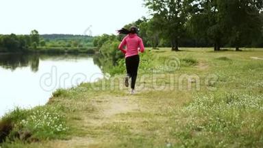 一个穿着粉红色夹克和黑色裤子的女孩戴着耳机在河边跑步，为<strong>马拉松</strong>做准备