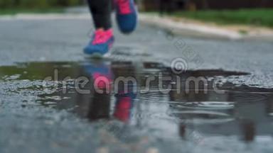 穿运动鞋的跑步者的腿的特写镜头。 女运动员在公园里慢跑，踩在泥泞的水坑里。