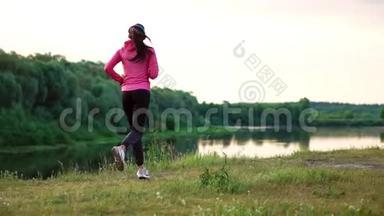 一个穿着粉红色夹克和黑色裤子的女孩戴着耳机在河边跑步，为马拉松做准备