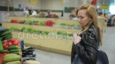 一个女人在<strong>超市</strong>的蔬菜货架上买蔬菜和<strong>水果</strong>，