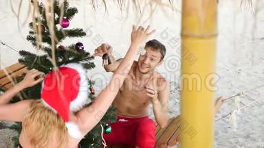两个戴着<strong>圣诞</strong>帽的男人和女孩在海滩上<strong>迎</strong>接新年和<strong>圣诞</strong>节。 把<strong>圣诞</strong>树装饰在<strong>圣诞</strong>树上