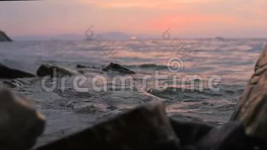 特写慢动作低角度小海浪在岩石海滩上翻滚.. 海边。 傍晚在卵石岩石海滩上日落