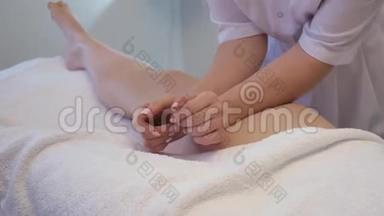 年轻女子在美容院做脚部按摩。 玛瑟揉捏一个年轻漂亮女孩的脚和腿。 关闭