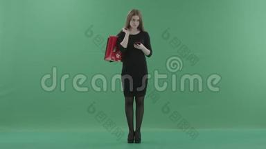 穿着小<strong>黑裙子</strong>的美女正在手机上发短信或上网，手里拿着她的购物