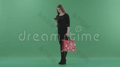 穿着小黑裙子的美女正在手机上发短信或上网，手里拿着她的购物