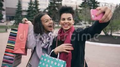两个可爱的非裔美国女人带着购物袋和微笑自拍。 朋友们在参观商场销售后玩得很开心。